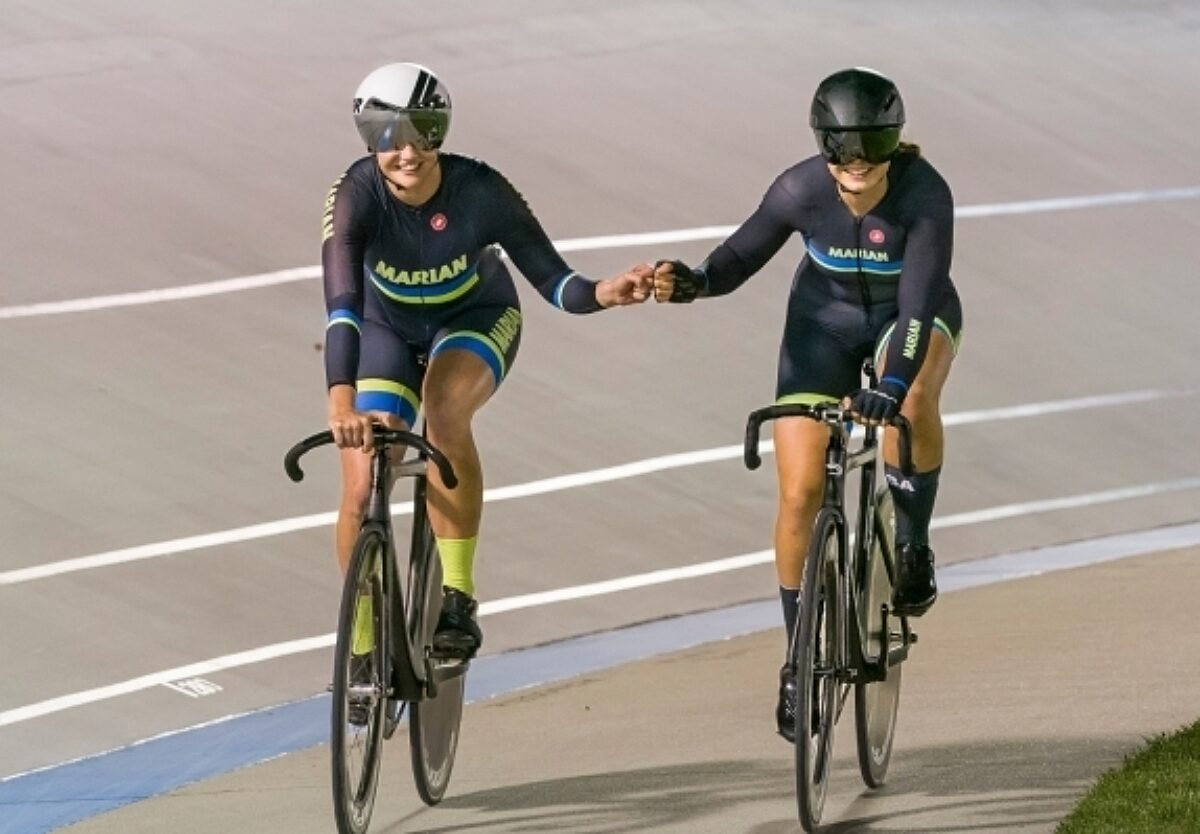 Two female bikers giving each other a fist bump while riding side by side.