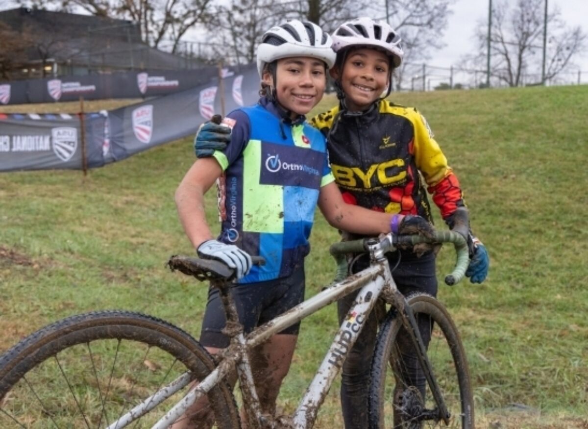 Two young cyclists holding a muddy gravel bike at a USAC bike race