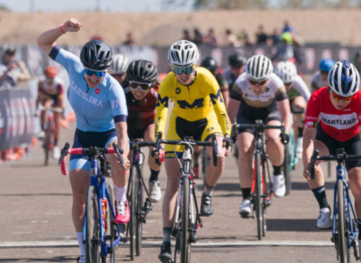 Collegiate female celebrating winning a road race while still on her bike.